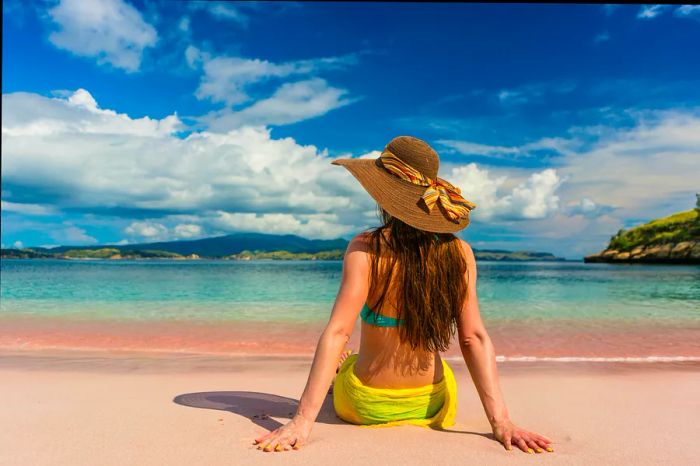 A young woman wearing a straw hat relaxes on the sandy shores of Pink Beach, Komodo Island, Indonesia