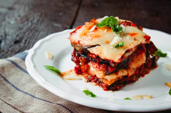 Traditional Parmigiana di melanzane: baked eggplant - a classic of Sicilian cuisine. This dish features layers of eggplant, cheese, and tomatoes, elegantly presented on a white plate, with a rustic backdrop of a wooden table.