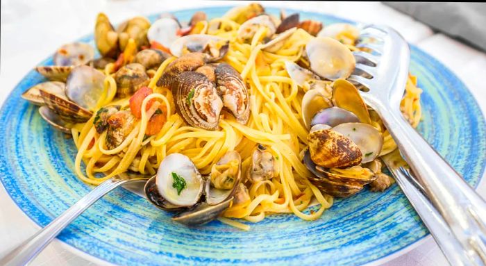 A plate of spaghetti with clams elegantly presented on a white tablecloth.