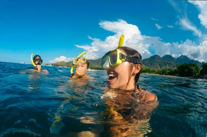 Three women floating on the water, equipped with snorkeling gear and sharing laughter