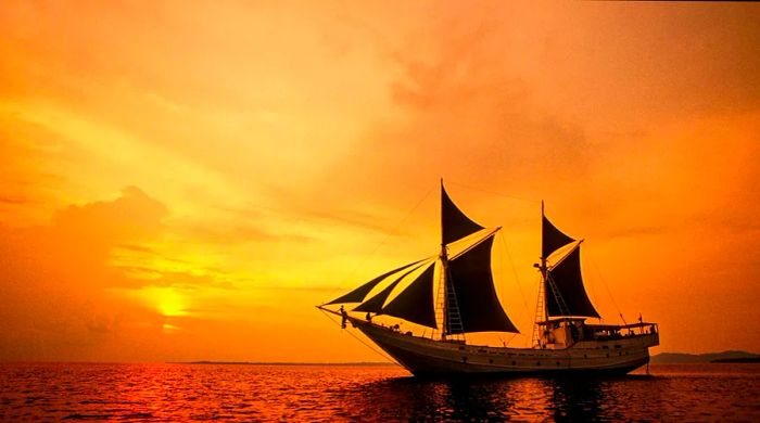 A Bugis-style phinisi schooner sails against the sunset in the Mentawai Islands, Indonesia.