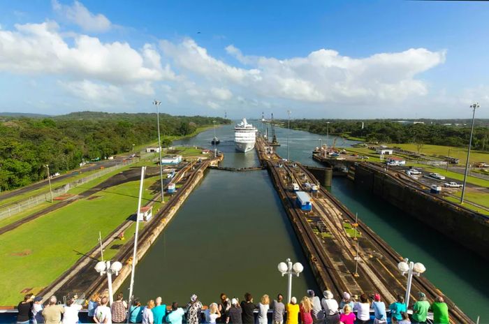 A crowd watches as a cruise ship approaches through a narrow channel of the Panama Canal.