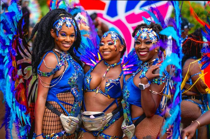 Three cheerful women in vibrant blue carnival outfits at Crop Over in Barbados.