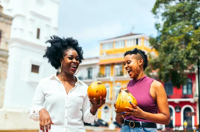 Stylish friends enjoying a walk on the streets of Panama City, sipping fresh coconuts.