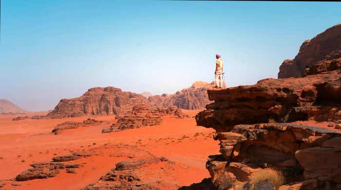 A young man stands on a cliff overlooking the Wadi Rum desert in Jordan, Middle East