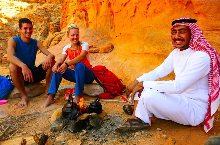 Two tourists enjoy tea with their Bedouin guide in the stunning Wadi Rum, Jordan.