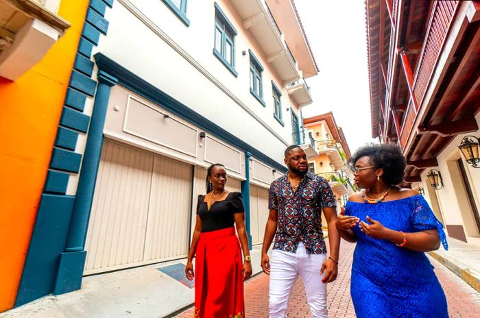 Wide-angle view of a stylish Afro-descendant woman leading a walking tour for a well-dressed couple in the Huerta Sandoval neighborhood of Panama City.