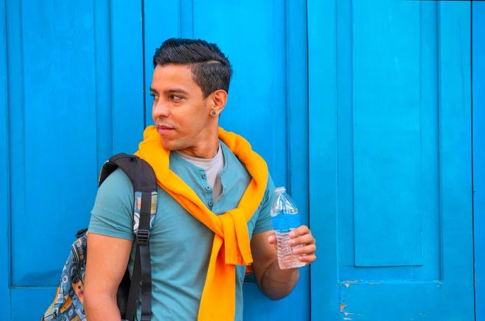 Young Hispanic men standing by a blue door with a bottle of water, Panama.