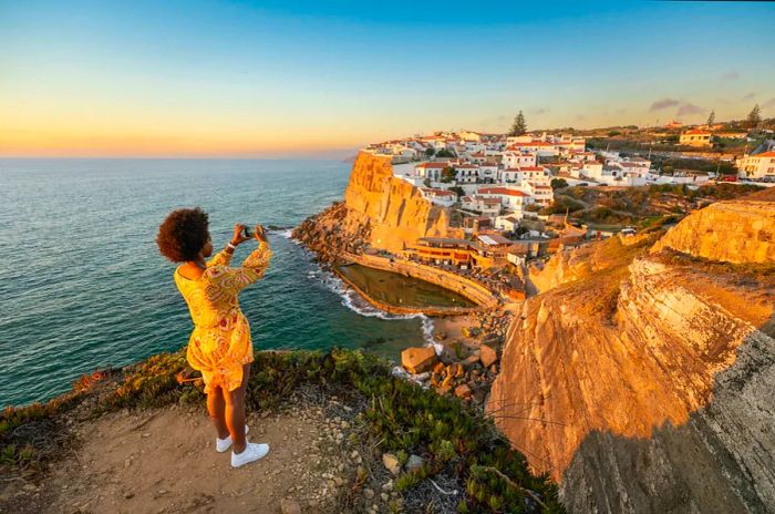 A woman captures a photo of Sintra, Portugal from a scenic cliffside