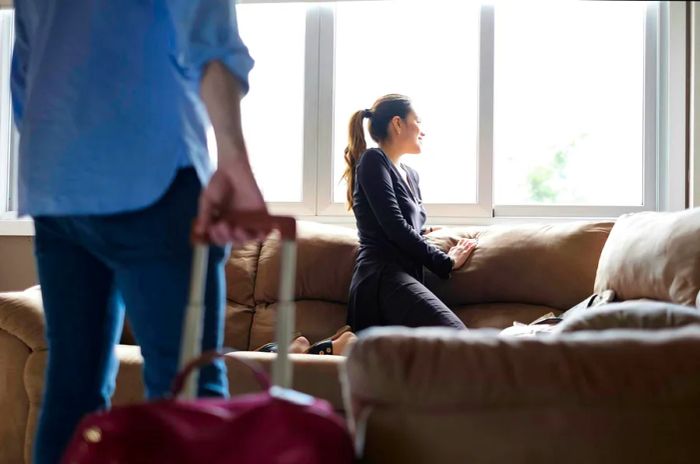 A couple enjoying a spacious hotel room in Panama, with the woman gazing out the window while the man handles a red suitcase.