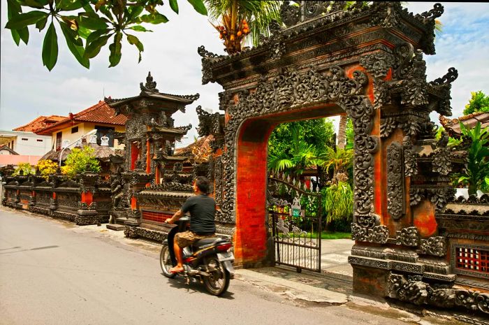 A man rides a scooter past the entrance of a Balinese temple