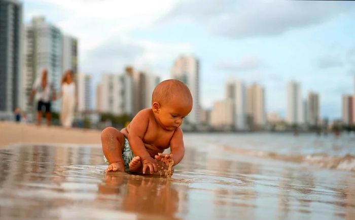 A baby plays joyfully in the sand at a beach in a resort town.