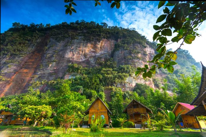 A collection of wooden huts nestled at the base of a towering cliff in the jungle