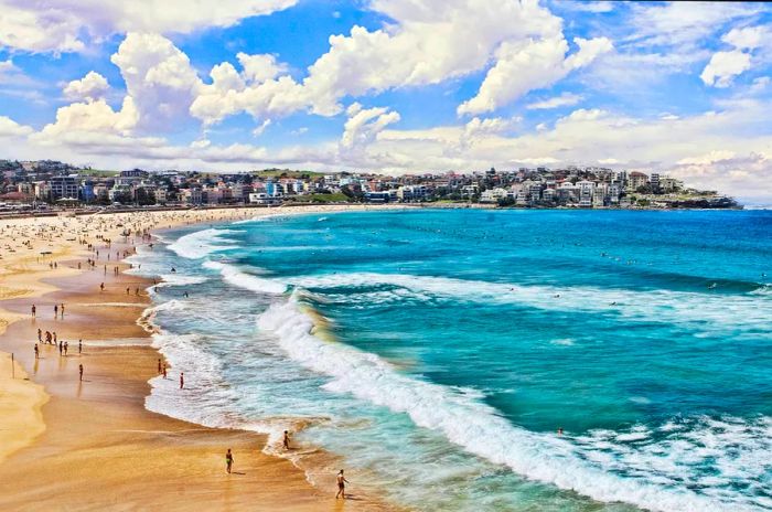 The sweeping curve of a beach with waves crashing against the shore and people enjoying the sand.