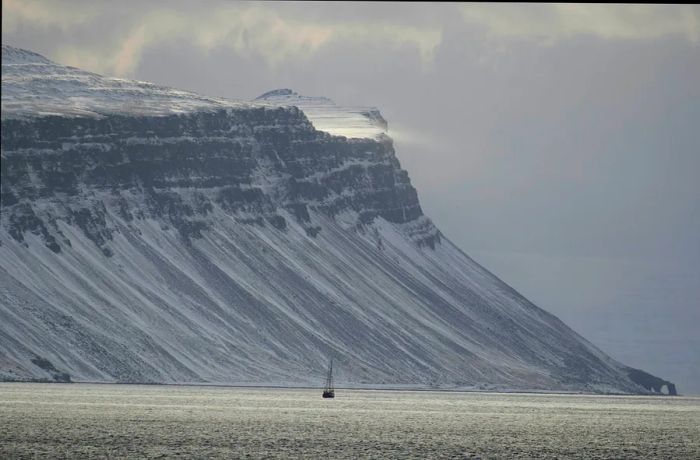 A mountain looms with a sailing boat drifting in the foreground at Hornstrandir Nature Reserve, Westfjords, Iceland