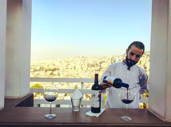 A bartender serves a glass of local Jordan River Shiraz while offering a view of Amman from the upper terrace of Cantaloupe.