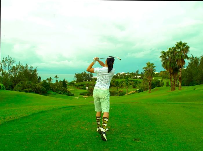 A woman takes a swing on a golf course in Bermuda on a cloudy day.