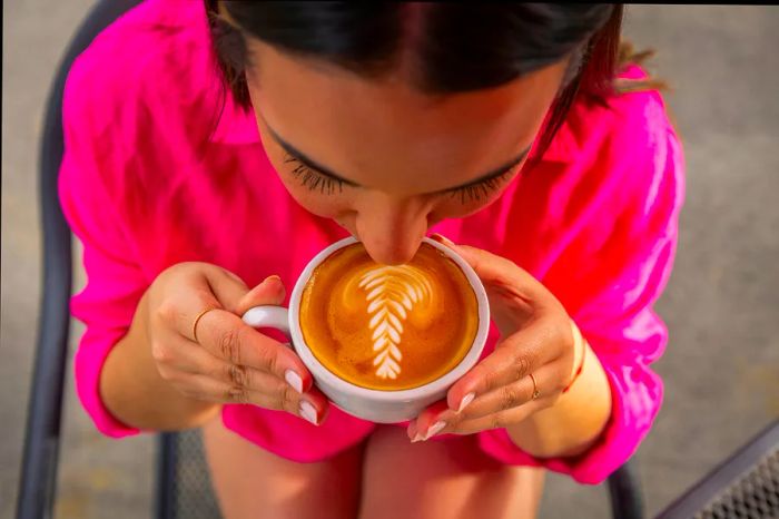 A young woman in a vibrant pink shirt gazes down at her cup while enjoying a coffee at Hacienda Munoz, Puerto Rico.