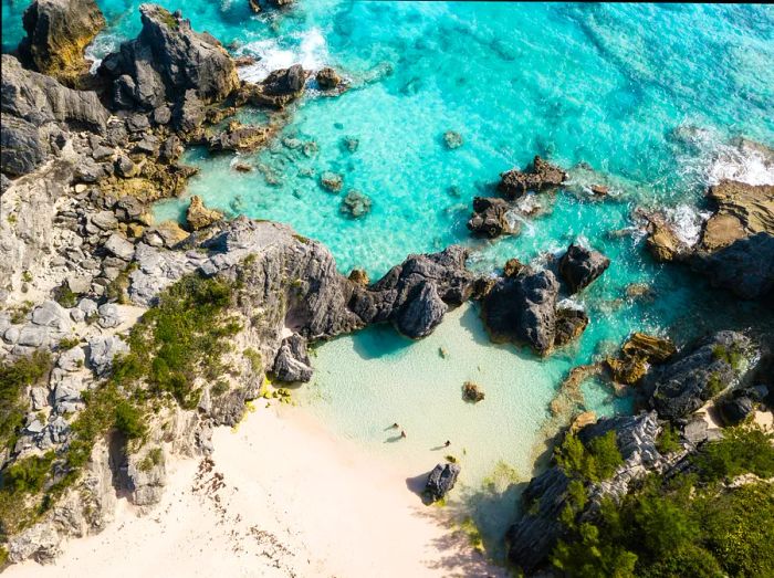 Aerial view of a rocky cove in Bermuda with two individuals on the shore