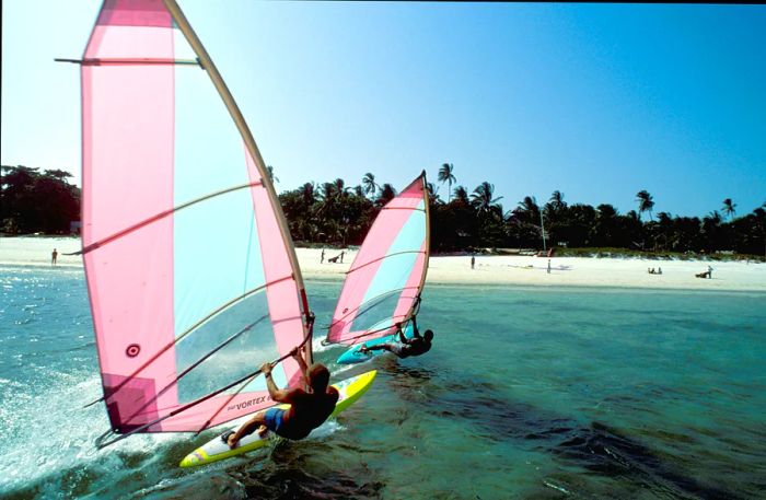 Two individuals windsurfing in the waters near a beach resort close to Mombasa