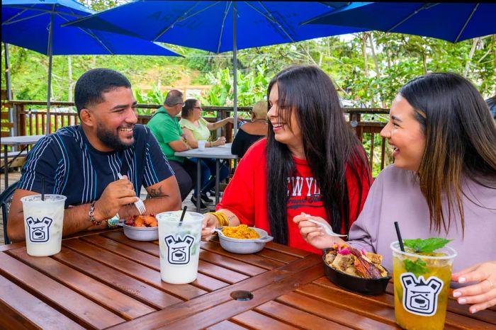 A man and two women enjoy food and drinks at an outdoor table in Cayey, Puerto Rico.