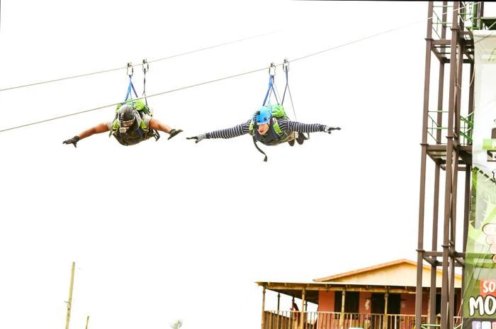 Two men stretch their arms wide while ziplining down a high line.