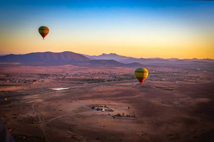 Hot-air balloons ascend over a landscape painted in shades of red as the sun rises.