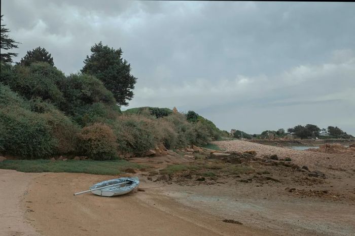 A small boat on an isolated beach along the Breton coast, with homes dotting the shore