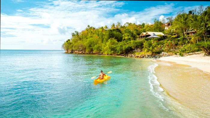 A man kayaking in a bright yellow kayak on a tropical St Lucia beach in the Caribbean.