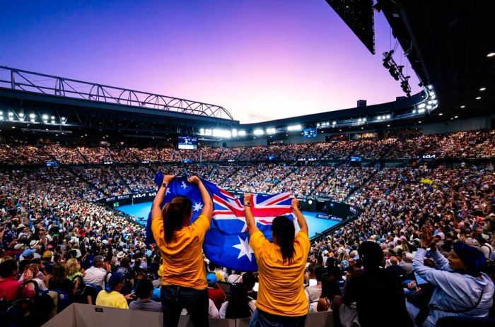 A couple stands out in a crowd at a tennis event, waving an Australian flag