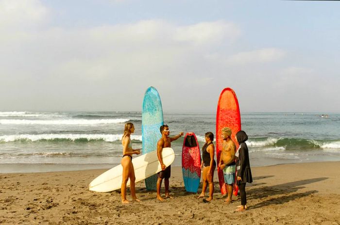 A small group of four surfers receives guidance on a beach.