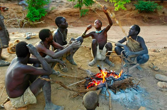 Hadzabe tribesmen gathered around a fire with their bows and arrows.