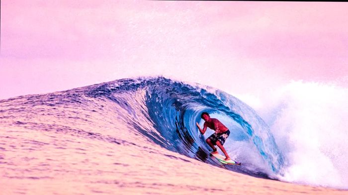 A surfer rides a wave in the Indian Ocean, framed by a pink sky