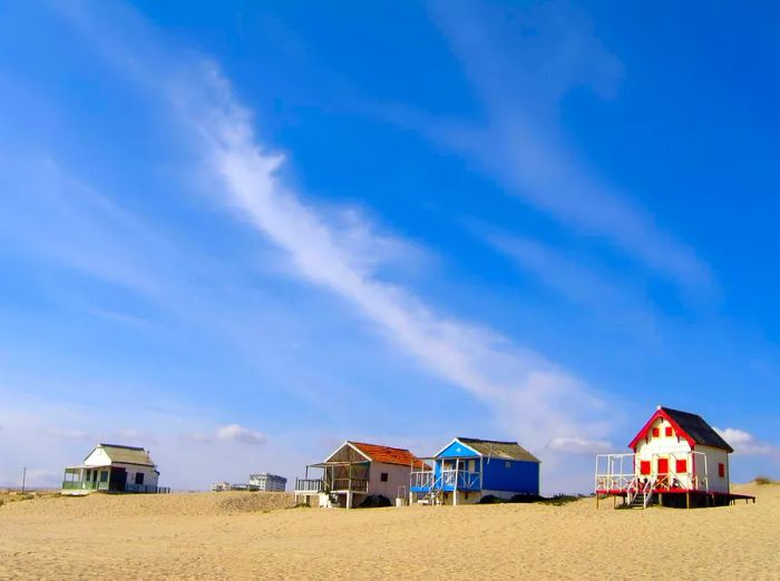 Wooden beach huts line a golden sandy shore.