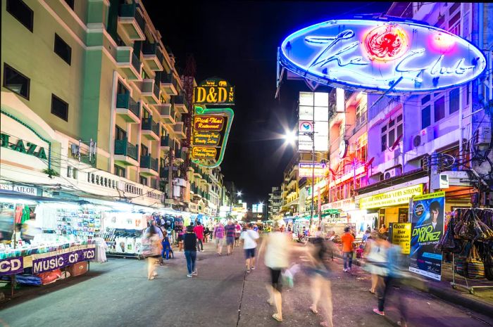 Blurred figures stroll along Khao San Road at night, a hotspot for backpackers and travelers.