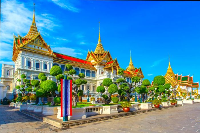 The golden stupa of the Grand Palace, Wat Phra Kaew, glistens against a clear blue sky in Bangkok, Thailand.