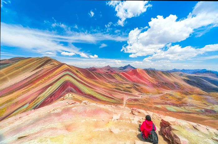 A female tourist enjoys the view of the vibrant, striated peaks of Vinicunca, also known as Rainbow Mountain.