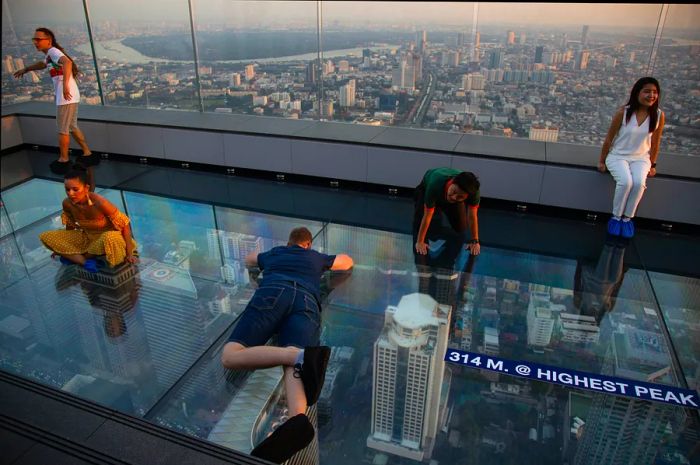 Visitors relax on the glass floor of the rooftop at the King Power Mahanakhon building in Bangkok, gazing at the glittering city skyline below.