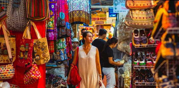 A young Asian woman strolls with headphones through the bustling stalls of Chatuchak market.