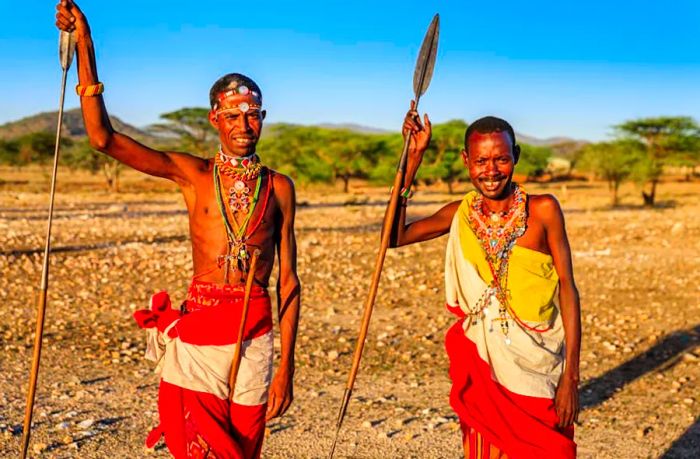 Two Samburu men dressed in traditional attire hold spears and pose for the camera.