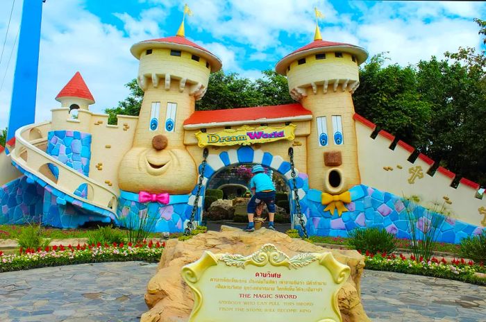 The entrance to Dream World amusement park in Bangkok features a whimsical castle adorned with large, cheerful faces as a child prepares to step inside.