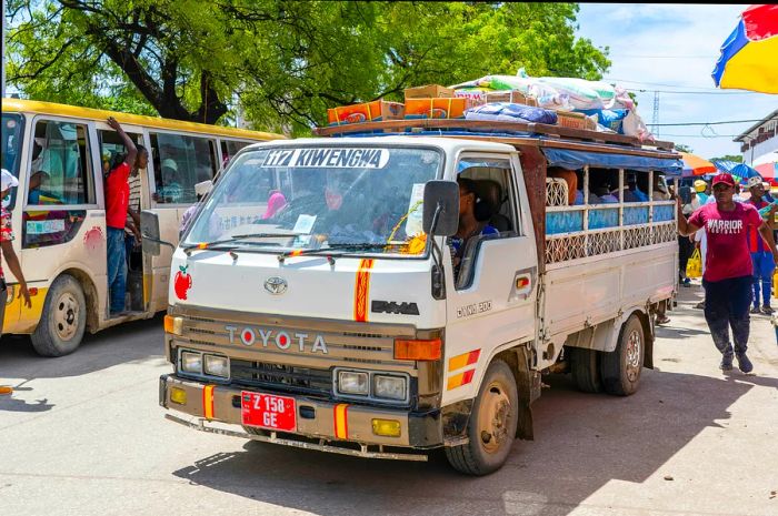 A Dala dala bus navigating the streets of Tanzania, surrounded by other forms of public transport, passengers, and pedestrians in the background