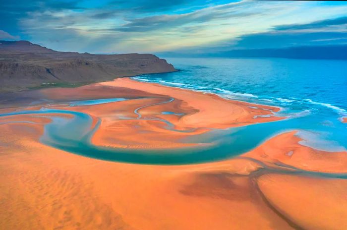 Aerial view captured by drone of Iceland's Raudasandur beach showcasing its azure water streams and golden sands.