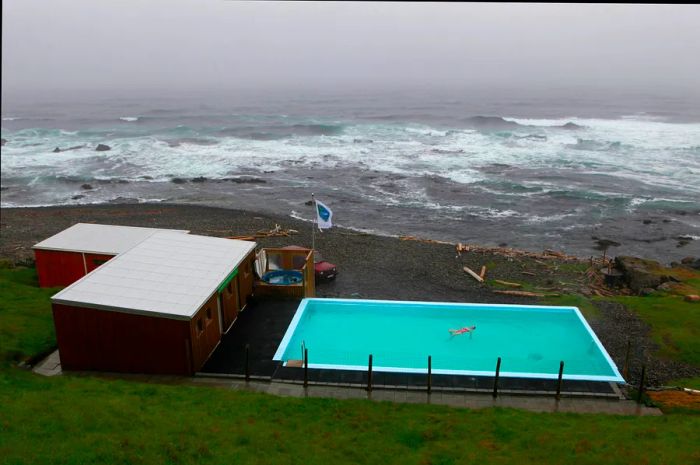 A woman relaxes in a hot spring in her garden, adjacent to a black sand beach at Krossneslaug, Westfjords.