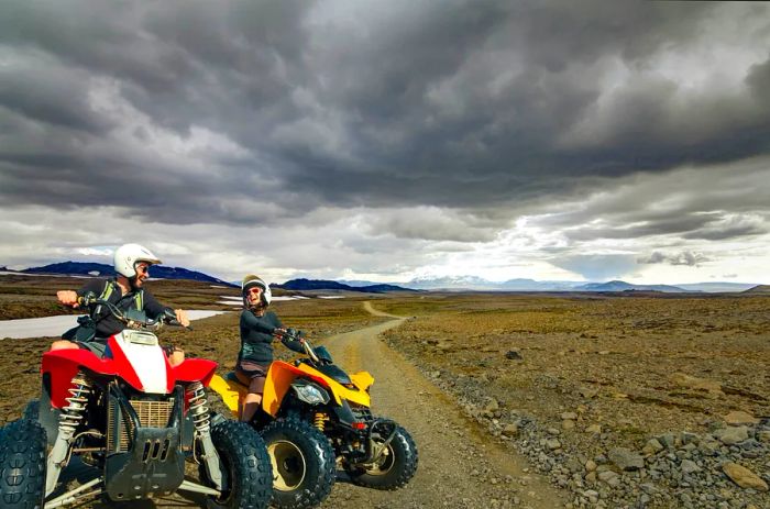 A joyful young couple rides ATV quad bikes, smiling as they navigate the rugged Icelandic highlands along the dirt road F550 in Kaldidalur, Iceland.