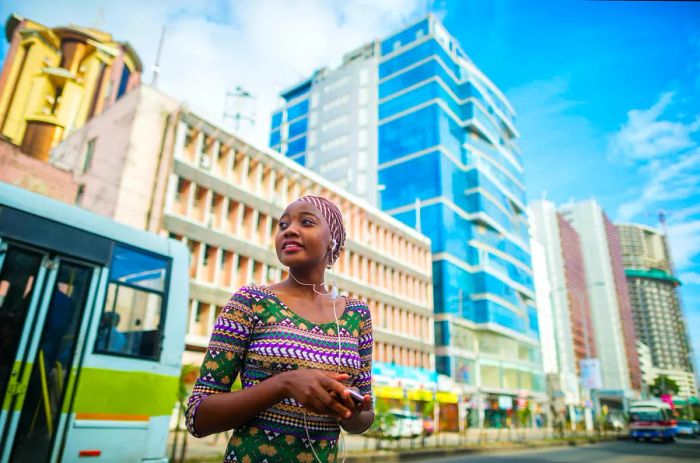 A young African girl listens to music, glancing over her shoulder while standing in the city center as a bus passes by in Dar es Salaam, Tanzania