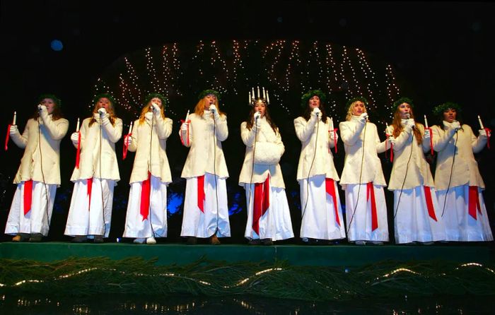 a group of women dressed in white robes with wreaths singing on stage