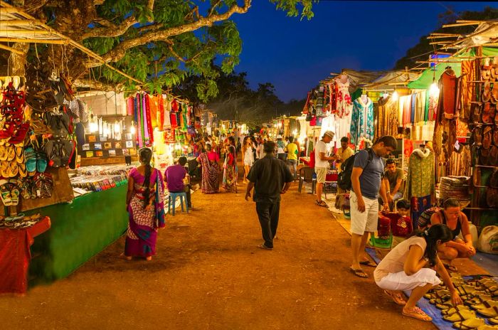 Numerous shoppers browse through clothes, shoes, and textiles at the stalls in Goa Night Market, Goa, India.