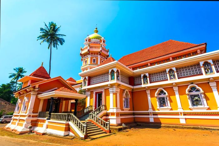 Shree Shantadurga Temple in Goa, India, vividly painted in bright yellow-orange against a clear blue sky.