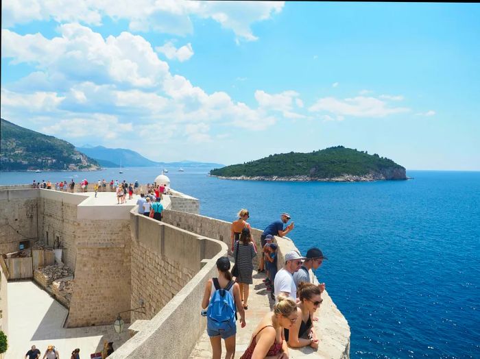 Tourists enjoying the views from the city wall in Dubrovnik's Old Town on a sunny day.